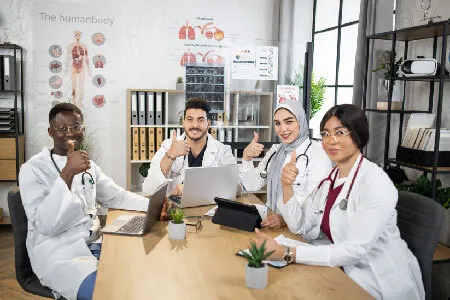 A stock photo of a team of doctors around a table, all giving a thumbs up.